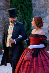 A woman and a man, elegantly dressed, in 19th-century style clothes, walk and chat in the courtyard of a palace