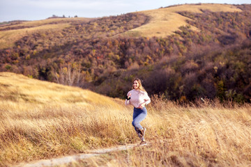 Naklejka na ściany i meble Woman in sportware running in the nature with dry grass and glade on background