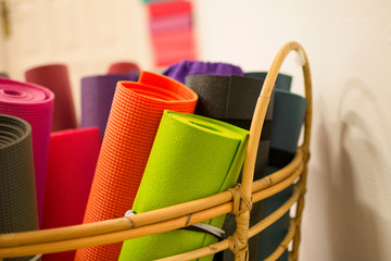 Wicker basket with several yoga mats or rolled pilates of different colors.