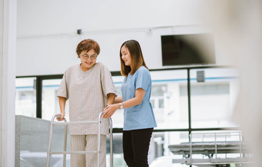 young physical therapist helping senior patient in using walker during rehabilitation