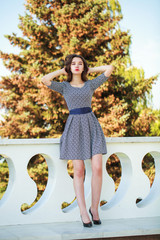 Full-length portrait of a young brunette woman in dress posing summer street
