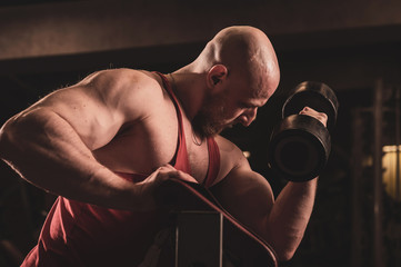 Fototapeta na wymiar Bald cute man with a beard is doing biceps exercise. The young guy is engaged in bodybuilding. Trainer in the gym with muscular arms.