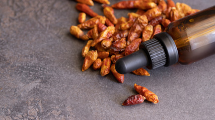 Chilli pepper essential oil and dried chilli peppers  on cocnrete background for beauty and natural medicine.