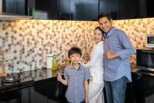 Beautiful Young Asian Woman Mother With Man Husband And Young Boy Son Family Washing Dishes In Modern Kitchen Room, Looking At Camera, With Thumb Up