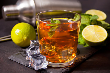Fresh cocktail Cuba Libre with brown rum, cola, mint and lime on black background. Long Island Iced Tea cocktail.