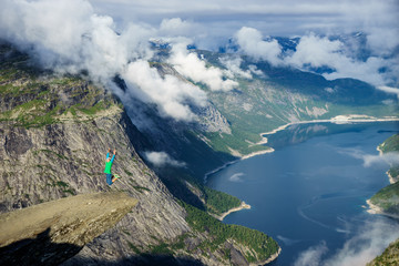Naklejka na ściany i meble Young man jump on the edge Trolltunga. Norway