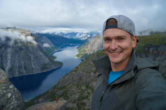Young traveller taking selfie on the top with Beautiful fjord on background in Norway