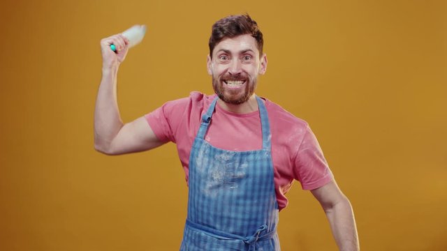 Jealous bearded husband baker hitting with rolling pin angry threatening furious severe face expressions on background. Crazy chef. Funny scene.
