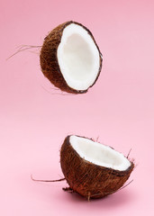 Two coconut section halves isolated on pink background one broken in two. Levitation composition.