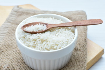 Natural raw white rice grains, on display in bowl and wooden spoon