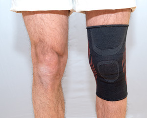 black elastic bandage on an injured knee on a light background