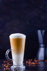Latte macchiato in a tall glass. Glass of coffee latte and coffee beans on a dark background. Сopy space