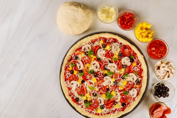 Raw supreme pizza with ingredients during making.