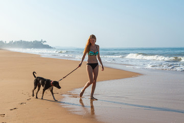 Beautiful young girl walks with dog along the beach of the ocean