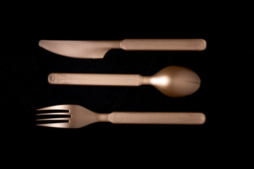 Close up of shiny dark gold coloured plastic cutlery set of horizontally ordered knife, spoon and fork laying face down