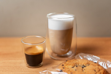 Cappuccino and espresso in transparent double-bottomed glasses near cookies on a wooden table close-up.