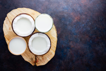 Coconut milk and coconut in paper glass on dark background. Coconut vegan milk non dairy on a wooden stand. Healthy drink concept. Alternative milk. Top view