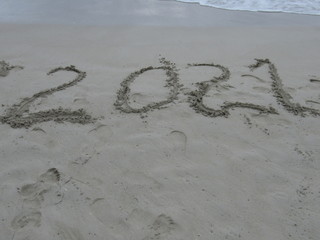 Happy New Year 2021, lettering on the beach with wave and clear blue sea. Numbers 2021 year on the sea shore, message handwritten in the golden sand on beautiful beach background. New Years concept.