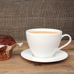 cappuccino coffee in a white cup and saucer and chocolate muffin in paper on an old wooden table, dark background, concept of sweet life