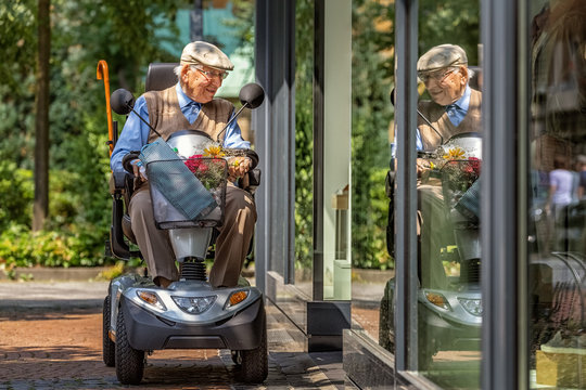 An elderly person on an electric vehicle looks into a shop window