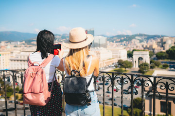 Europe travel summer tourism holiday vacation background - two girls friend with hat mobile cell phone and using backpack in hand taking selfie photo and filming blog