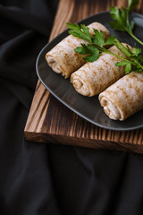 Stuffed pancakes with meat filling decorated with parsley, on a wooden board. Dark background