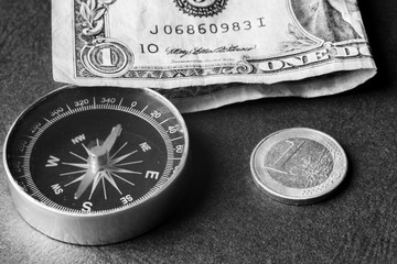 dollar, euro coin and compass on black paper surface. black and white color