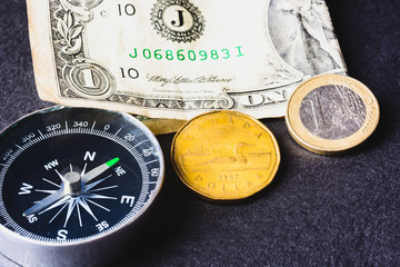 american dollar, canadian dollar, euro coin, compass and boat on a black background