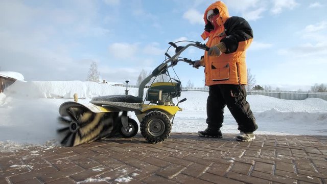 Man cleans snow in the yard with a sweeper in the winter