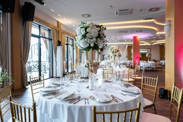Table at a luxury wedding reception. Beautiful flowers on the table. Serving dishes, glass glasses, waiters work.