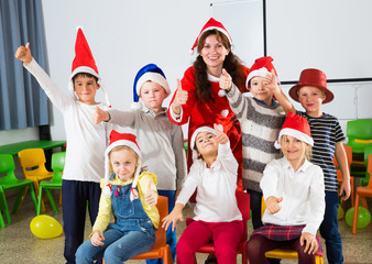 Obraz premium Pupils with teacher in Santa hats giving thumbs up