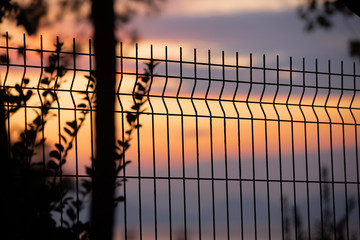 View of the sea sunset through the fence of the guarded territory. Blur, selective focus. Overnight at the hotel by the sea.