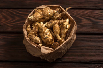 Several Jerusalem artichoke tubers in a paper bag on a wooden table with copy space. Helianthus tuberosus. Top view