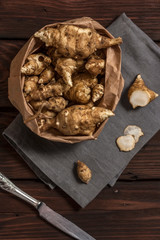 Several Jerusalem artichoke tubers in a paper bag on a wooden table with copy space. Helianthus tuberosus. Top view