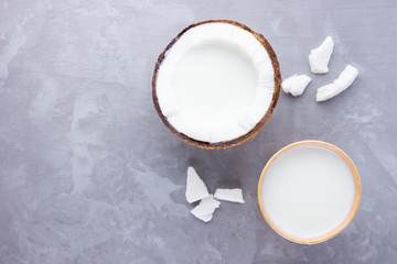Obraz na płótnie Canvas Coconut milk and coconut in paper glass on gray background. Coconut vegan milk non dairy on cement. Healthy drink concept. Alternative milk. Top view