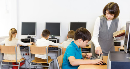 Fototapeta premium Female teacher working with schoolboy in computer class