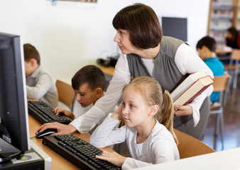 Fototapeta premium Woman teacher helping tween girl in computer class