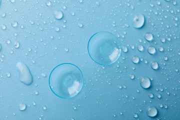 Contact lenses on blue background with water drops, top view