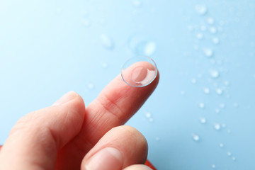 Female hand holds contact lens on blue background, close up