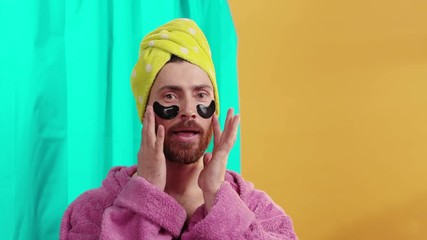 Funny-looking tbearded man transgender looking in the mirror wearing eye patches cleaning face caring smile happy posing in the bathroom. Orange background.