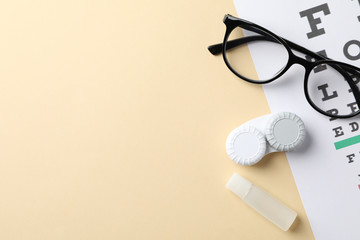 Glasses, contact lenses and eye test chart on beige background, top view