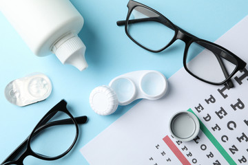 Glasses, contact lenses and eye test chart on blue background, top view