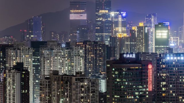 Day to night timelapse of downtown apartment buildings pan down. Chinese crowded city overnight. Fast paced modern Asian night-scape time lapse in urban metropolis of Shenzhen.