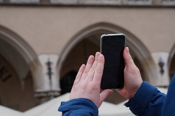 Hand of tourist holding mobile smartphone with black screen on the background of an old house, photographing sights or architecture. Journeys or Travel concepts and technology