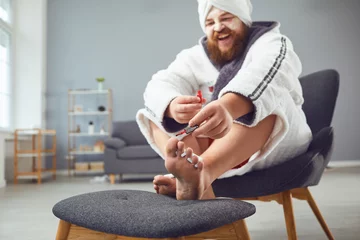 Foto op Canvas Grappig pedicureconcept. Grappige dikke man in een badjas en een handdoek lakt zijn nagels © Studio Romantic