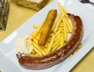 Tasty rustic sausage with french fries served at plate with white sauce