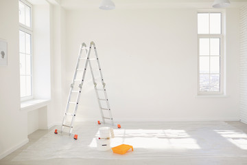 Painting in a white room with windows with a stepladder
