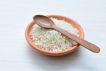 Natural raw white rice grains, on display in bowl and wooden spoon
