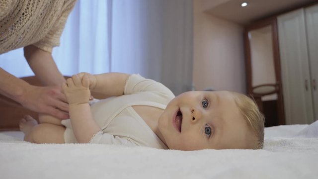 Careful mother changes baby diaper at home. Cute toddler with blue eyes lies on a diaper in bedroom. Mom and toddler concept of a happy childhood. Low-angle shot in close-up