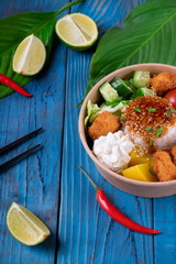 Poke bowl with fried chicken, vegetables and rice on the blue wooden background. Hawaiian cuisine meal